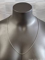 Full view of the silver necklace displayed on a mannequin showing the length and delicate twisted rope design.
