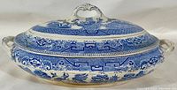 View of the covered oval casserole showing its blue and white Blue Willow decoration, decorative handles on lid and sides, and signs of stained crazing on surface.