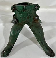 Close-up of green painted cast iron Christmas tree stand, showing embossed 'A Very Merry Xmas' text and attachment screws.