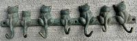 Cast iron coat hook showing seven cats with curled tails serving as hooks, displayed on a textured surface.