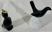 Two porcelain pie birds, one black with beige spout and tapered body, and the other glossy black on white circular base.