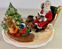 Side view of the Santa Claus tealight candleholder with Santa seated reading a book, children nearby, Christmas tree with ornaments.