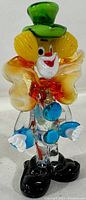Front view of hand blown Murano glass clown figurine with green top hat and yellow bow tie.