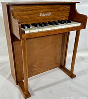 Full front and side angled view of the miniature Schoenhut toy piano showing keyboard, legs and wood grain finish.