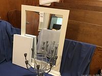 The mirror with white frame, the floating shelf laid in front, the glass vase, and the metal candelabra with eight candle holders.