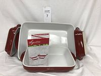 Four Lagostina stoneware casserole dishes in various sizes, three with lids and one without, red exterior and white interior, showing clean and like-new condition with product pamphlet.
