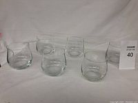 Photo shows six clear glass highball glasses arranged in two rows of three against a plain background.