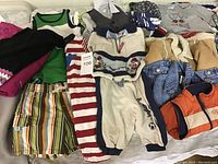 Top view of assorted baby clothes including tops, pants, outerwear, and bodysuits in various colors and patterns.