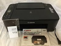 Canon PIXMA TS3129 printer shown with power cord and user manuals placed in front.