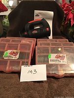 Cut-out saw with nine red-latched, stackable transparent plastic storage boxes containing assorted hardware, with a display card labeled '143' in front.