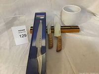 Photo showing all items in the lot including boxed JA Henckels Stylus knife, two Think Kitchen knives, ceramic holder, and wooden magnetic utensil bar