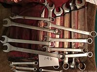 Mastercraft combination wrenches in various sizes laid out on a red fabric roll and brown fabric background, showing 12 different wrenches mostly in good condition with some wear.