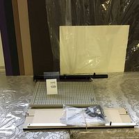 Photo of a paper cutter with grid base and cutting arm along with the mat cutting tool wrapped and secured with a rubber band, placed on a table beneath mat boards.