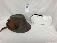 Brown fedora hat with feather and button embellishment, three pairs of Hanes white ankle socks packaged together on the right side, photo of lot on plain background.