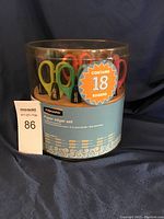 Complete set of 18 Fiskars paper edger scissors visible through clear plastic packaging, showing colorful handles and text details on box labeling the product and patterns.