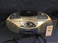 Front view of the Sanyo boombox showing speakers, control buttons, CD player lid, digital display, and power cord