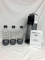 SodaStream Jet soda maker alongside three clear bottles and user manual, all placed on white background