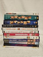 Stack of 12 DVD cases including TV shows The Big Bang Theory, Friends, and 10 romantic comedy movies such as Bridesmaids and 27 Dresses