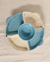 Top-down view of a ceramic appetizer dish and tray set with removable parts, showing four quarter-circle dishes alternating in blue and beige on a round tray, and a central round bowl in blue.