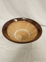 Top-down photo of handmade pottery bowl showing tan glazed interior with brown rim and speckled pattern inside.
