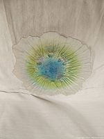 Top view of pearlescent floral glass plate showing blue, green, and pearl colors with textured petal edges.