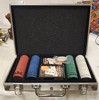 Poker set in open metal briefcase showing stacks of poker chips, two decks of cards, dealer button, and dice.