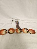 Five small decorative sauce bowls arranged in a row alongside packaged appetizer forks.
