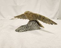 Side view of bird statue on stone base, showing extended wings and bird carved detail.