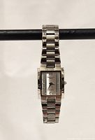 Front view of the stainless steel small rectangular wristwatch with a silver dial and link band, showing the brand name and date window at six o'clock.
