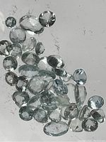 Multiple aquamarine gemstones displayed on a white surface, showing various cuts and sizes.