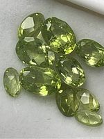 Close-up view of faceted peridot gemstones laid out on a white surface, showcasing their green color and clarity.