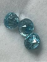 Three blue faceted zircon gemstones viewed closely showing cuts and color variation.