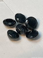 Six oval faceted dark blue natural sapphires on a white background, showing topside view and cut facets.