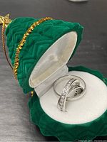 Set of three sterling silver rings displayed in a green velvet ring box with white interior lining, showing one ring with clear stones and two plain bands.