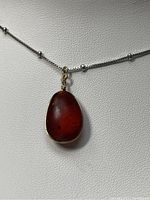Front view of amber pendant on silver necklace chain showing polished reddish-brown amber stone with wire wrapping.