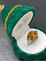Ring shown inside green velvet decorative box with gold trim.