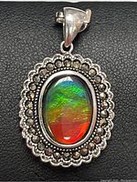 Front view of oval Ammolite gemstone pendant with marcasite set in sterling silver on black background.