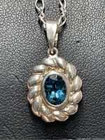 Close-up front view of a sterling silver pendant with an oval blue genuine gemstone in the center, surrounded by a twisted rope silver bezel, hanging from a silver chain.