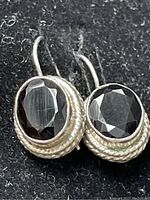 Close-up photo of front-facing oval black onyx stone earrings with textured sterling silver rope design encircling the stones, showing faceting and shine.