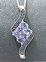 Close-up of sterling silver pendant with cluster of oval cut light to medium blue-violet tanzanite stones and smaller round tanzanite stones on sides.