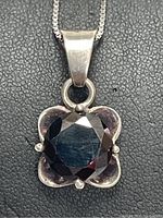 Close-up view of the silver pendant with faceted black onyx stone mounted in a four-petal floral design with visible prongs holding the stone.