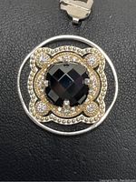 Close-up showing the front detail of the pendant centered on the faceted black onyx with the decorative circular frame and diamond-like stone accents.