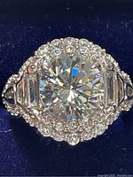 Close-up top angled view of sterling silver cubic zirconia ring with large round center stone, trapezoid side stones, and halo of smaller stones.