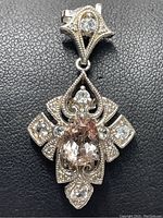 Front view of a sterling silver pendant displaying clear cubic zirconia stones and milgrain detailing on a textured black background.