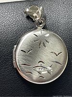 Close-up front view of circular sterling silver locket pendant showing detailed cutout designs of birds, fish, and star-like shape.