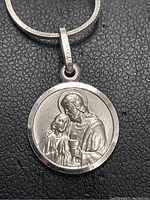 Close-up of the front of the round religious medal pendant showing saint and child figures in relief.