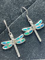 Pair of sterling silver dragonfly earrings with blue and green opalite inlay lying on black fabric background.