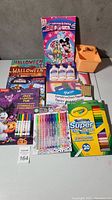 Lot contents showing Halloween coloring books, Crayola markers, gel pens, glue bottles, orange paint, and construction paper.