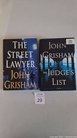 Two hardcover John Grisham books, 'The Street Lawyer' and 'The Judge's List' standing side by side on a flat surface, showing front covers.