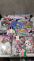 Lot of kids colouring books, sheets, and colouring supplies including markers, crayons, and coloured pencils all arranged on a table.